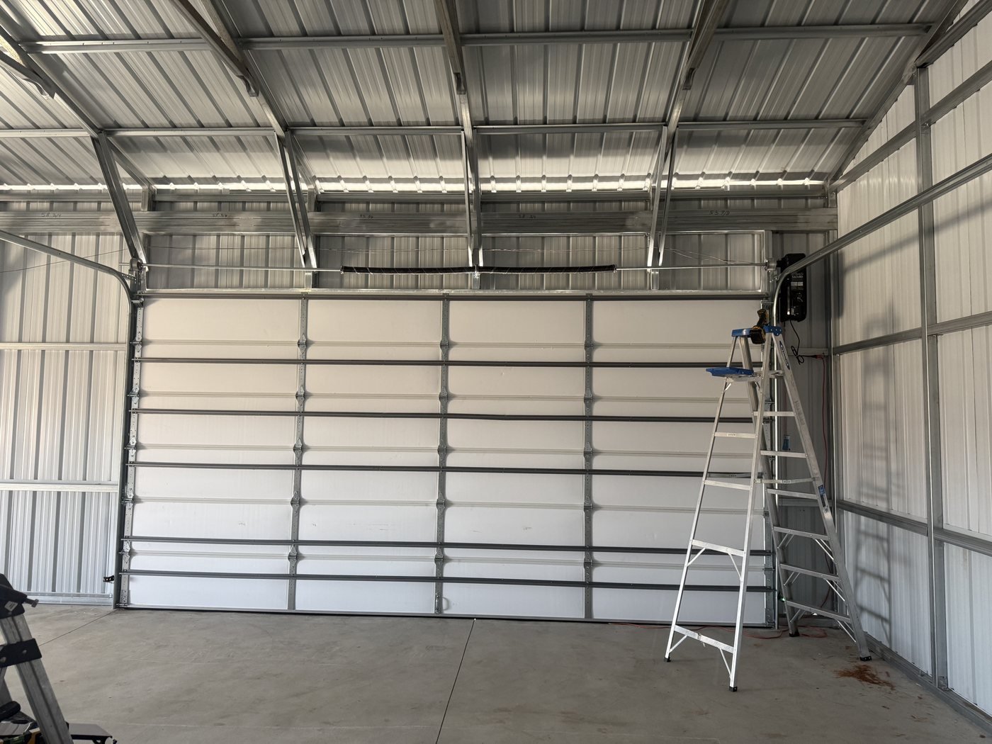 Interior view of a wide white commercial sectional door with tracks, counterbalance hardware and a side-mounted operator