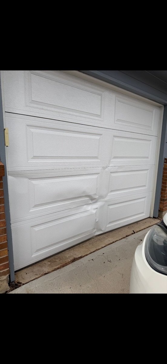 Bent and damaged white garage door panels viewed from inside a garage