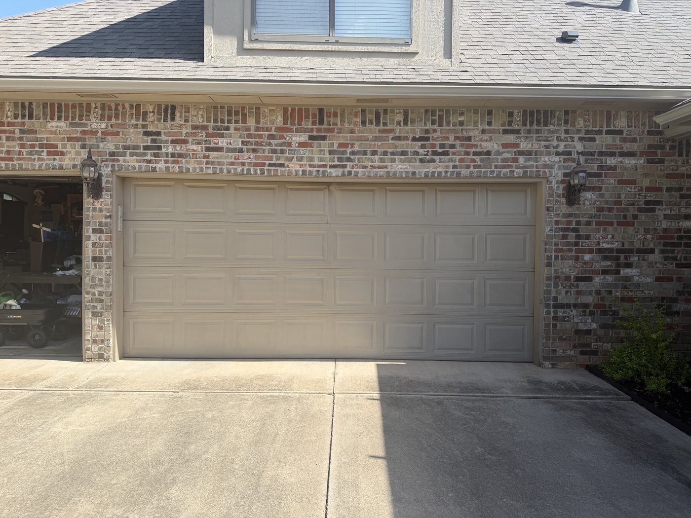 Tan raised-panel sectional garage door framed by brick
